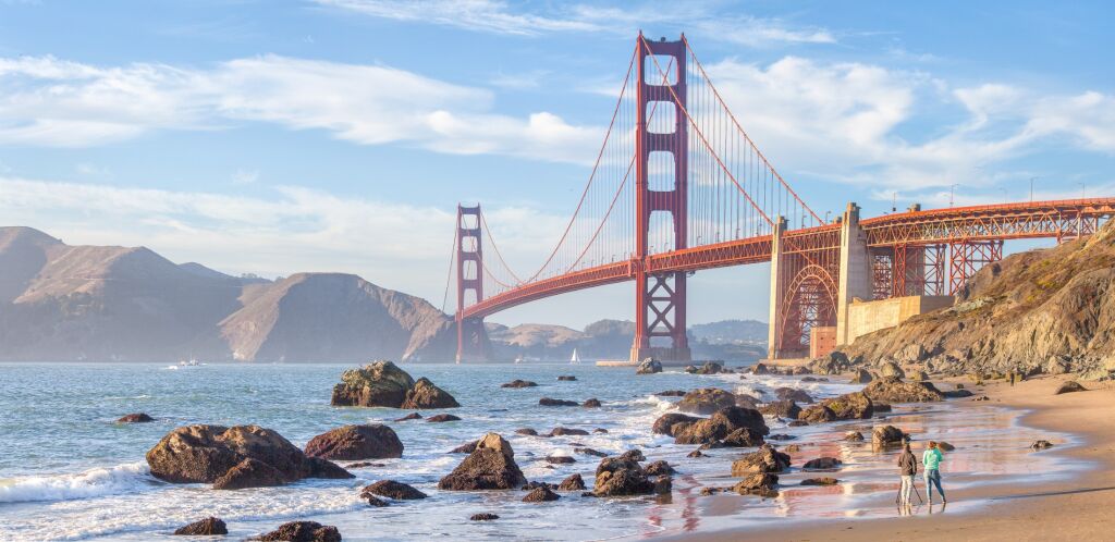 Klasyczny panoramiczny widok słynnego Golden Gate Bridge widziany z malowniczej plaży Baker w pięknym złotym świetle wieczorem w słoneczny dzień z błękitnym niebem i chmurami w lecie, San Francisco, Kalifornia, USA